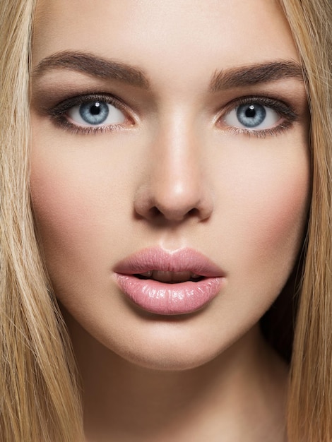 Photo gratuite portrait de jeune femme avec une peau saine d'un visage. jolie femme avec de longs poils raides et un maquillage brun. jolie fille magnifique aux yeux bleus - posant