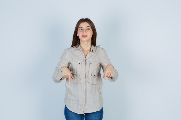 Portrait de jeune femme pointant vers le bas en jeans décontractés et à la vue de face optimiste