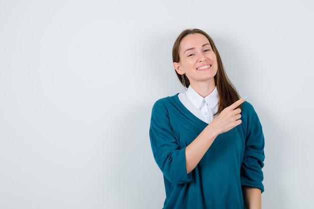 Portrait de jeune femme pointant vers le coin supérieur droit en pull sur chemise blanche et à la vue de face heureux