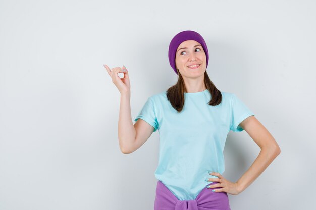 Portrait de jeune femme pointant vers le coin supérieur gauche en t-shirt, bonnet et à la vue de face de rêve