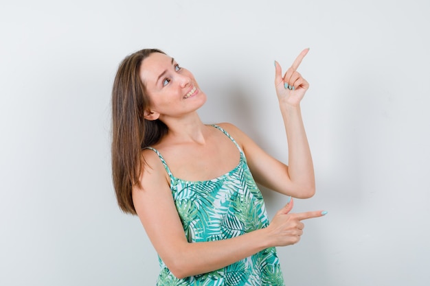 Portrait de jeune femme pointant vers le côté droit et le coin droit en blouse et regardant la jolie vue de face