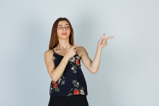 Portrait de jeune femme pointant vers le côté en haut floral et à la réflexion