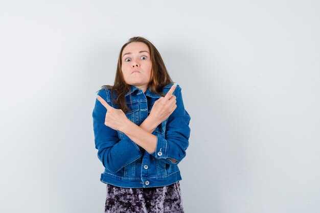 Portrait de jeune femme pointant vers les deux coins en blouse, veste en jean et à la vue de face sérieuse