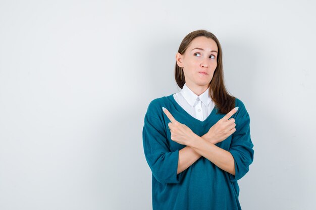 Portrait de jeune femme pointant vers la droite et la gauche, regardant de côté en pull sur chemise blanche et à la curieuse vue de face