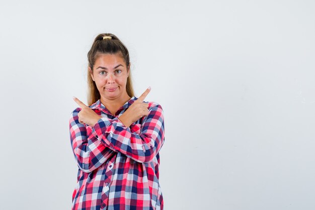 Portrait de jeune femme pointant vers le haut en chemise à carreaux et à la vue de face confiante