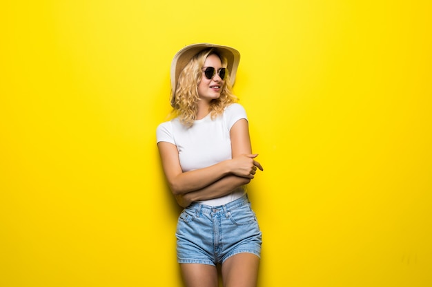 Portrait jeune femme portant un chapeau de paille posant sur un mur jaune coloré