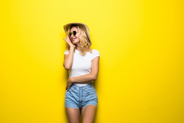 Portrait jeune femme portant un chapeau de paille posant sur un mur jaune coloré