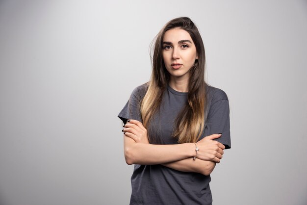 Portrait de jeune femme posant avec les bras croisés sur fond gris.