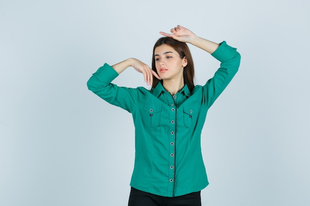 Portrait de jeune femme posant avec les mains autour de la tête en chemise verte et à la délicate vue de face