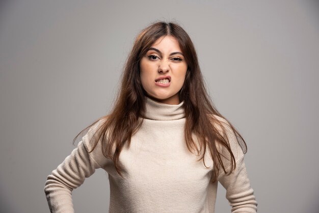 Portrait d'une jeune femme posant sur un mur gris.