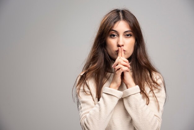 Portrait d'une jeune femme posant sur un mur gris.