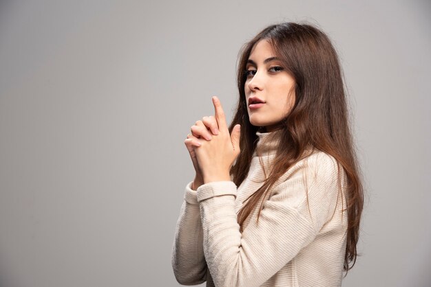 Portrait d'une jeune femme posant sur un mur gris.