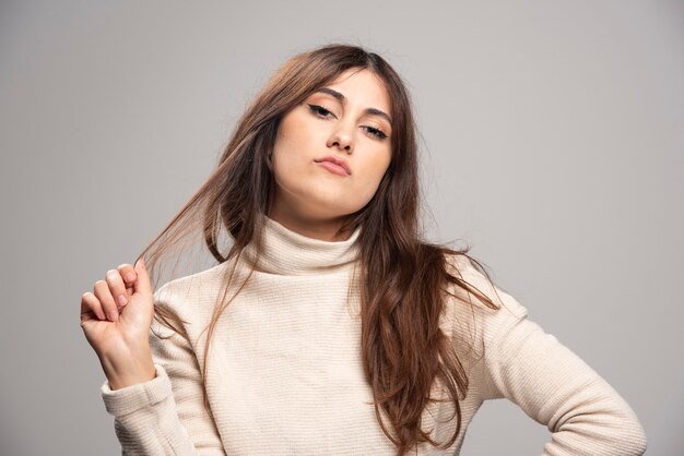 Portrait d'une jeune femme posant sur un mur gris.