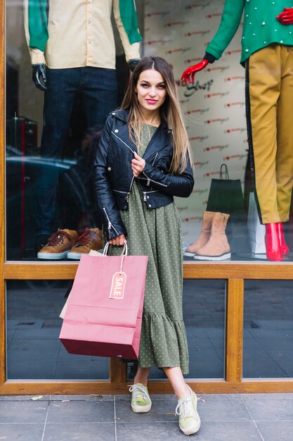 Portrait, jeune, femme, poser, devant, vitrine, tenue, sacs provisions, main