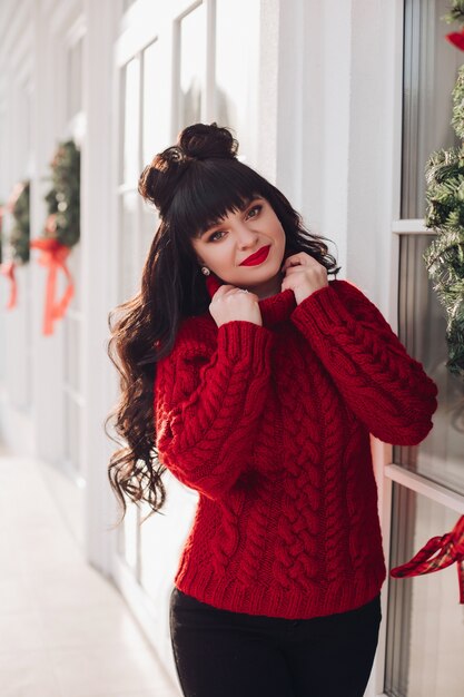 Portrait d'une jeune femme de race blanche dans un pull rouge tricoté chaud à l'extérieur sourires