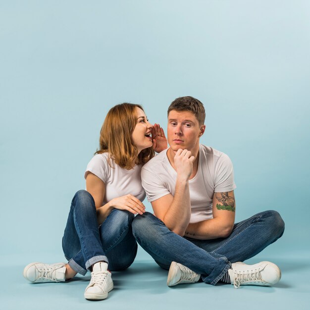 Portrait de jeune femme racontant un secret à son petit ami sur fond bleu