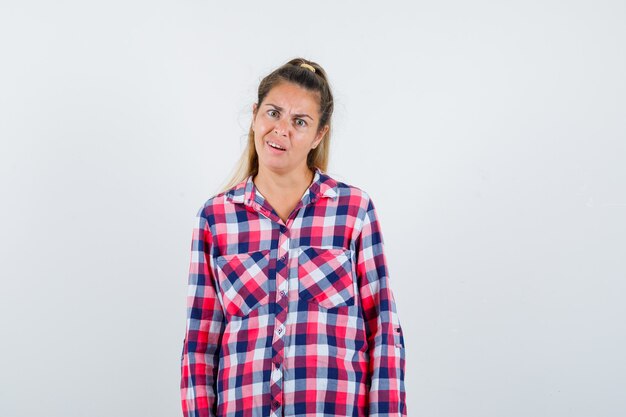 Portrait de jeune femme regardant la caméra en chemise à carreaux et à la vue de face confuse
