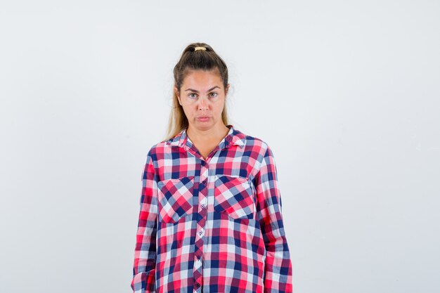 Portrait de jeune femme regardant la caméra en chemise à carreaux et à la vue de face douteuse