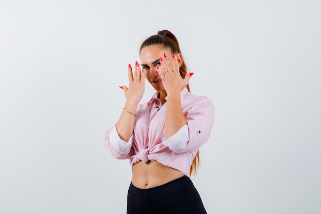 Portrait de jeune femme regardant à travers les doigts en chemise décontractée, pantalon et à la vue de face confiante