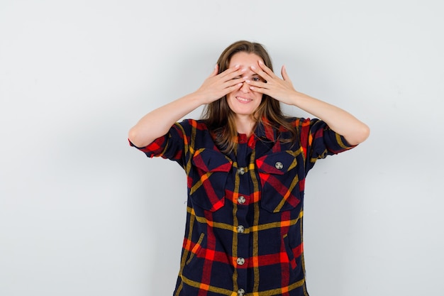 Portrait de jeune femme regardant à travers les doigts en chemise décontractée et à la vue de face curieuse