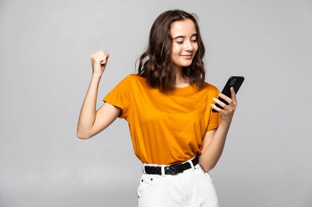 Portrait d'une jeune femme satisfaite tenant un téléphone mobile et célébrant isolé sur gris