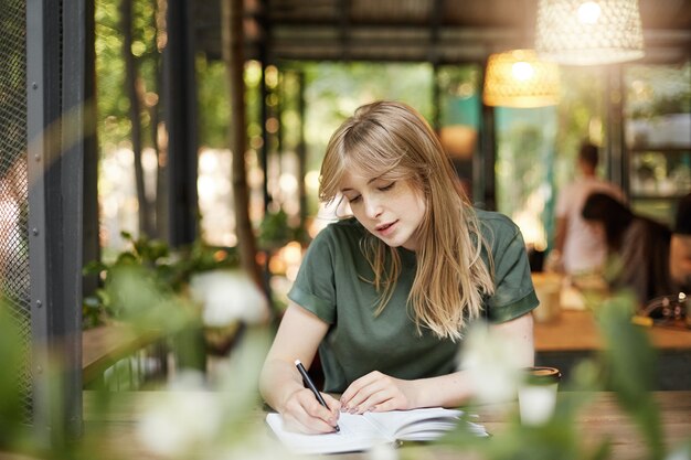 Portrait d'une jeune femme scénariste étudiante blonde écrivant son premier scénario dramatique de boire du café dans un café en plein air