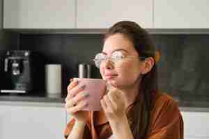 Photo gratuite portrait d'une jeune femme se reposant avec une tasse de thé, une fille buvant du thé dans la cuisine tient une tasse et regarde