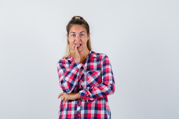 Portrait de jeune femme se rongeant les ongles en chemise à carreaux et à la vue de face en difficulté