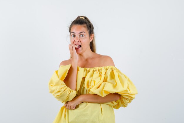 Portrait de jeune femme se rongeant les ongles en robe jaune et à la vue de face en difficulté