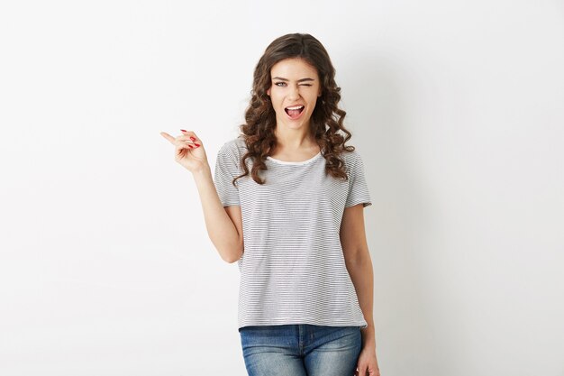 Portrait de jeune femme séduisante habillée en t-shirt et jeans tenue décontractée, pointer du doigt, un clin de œil, souriant, heureux, style hipster, isolé