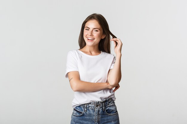 Portrait de jeune femme séduisante impertinente, jouant avec une mèche de cheveux et souriant satisfait.