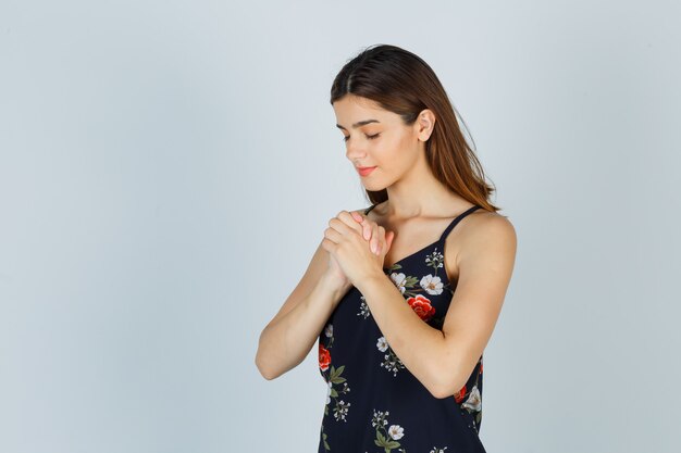 Portrait de jeune femme serrant les mains dans un geste de prière en chemisier et à la vue de face paisible