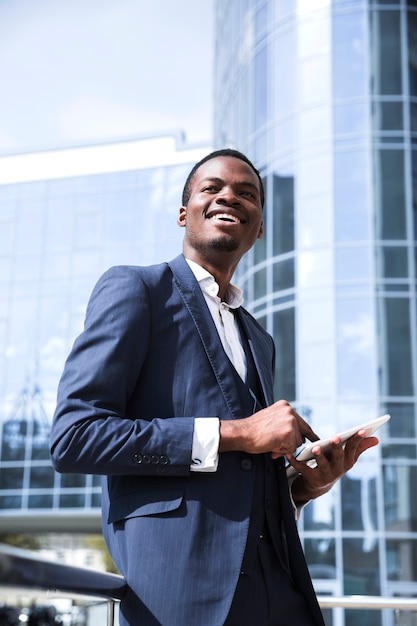 Photo gratuite portrait d'une jeune femme souriante à l'aide de tablette numérique devant l'immeuble de bureaux