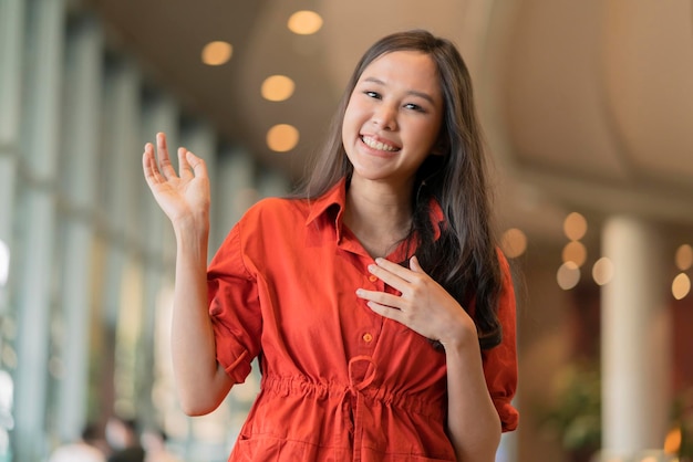 Portrait de jeune femme souriante asiatique gaie geste de la main pointer vers la surface debout dans le grand magasin du centre commercial avec arrière-plan bleu clair bokeh souriant femme asiatique tissu décontracté souriant caméra