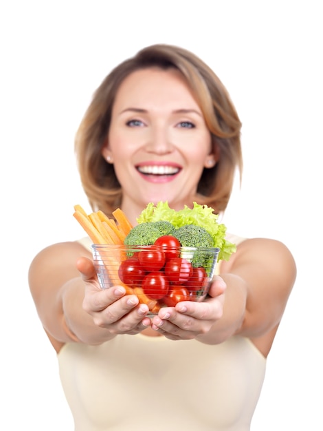 Portrait d'une jeune femme souriante avec une assiette de légumes isolé sur blanc.