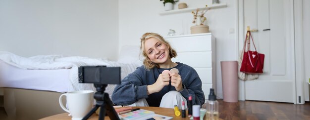 Portrait d'une jeune femme souriante assise devant une caméra numérique en train d'enregistrer une vidéo.