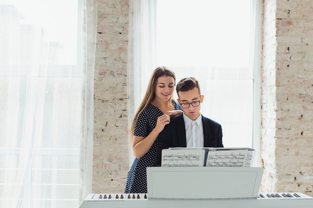 Photo gratuite portrait d'une jeune femme souriante, debout derrière l'homme jouant du piano près de la fenêtre