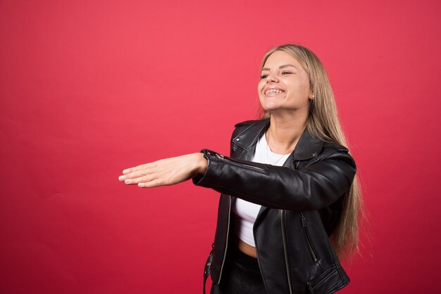 Portrait d'une jeune femme souriante étendant la poignée de main sur le mur rouge