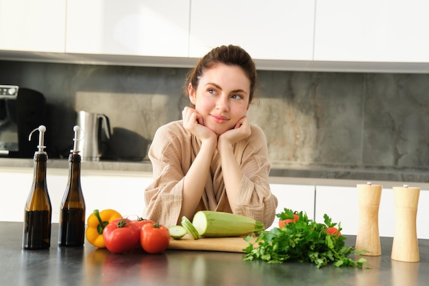 Portrait d'une jeune femme souriante s'appuyant sur le comptoir de la cuisine préparant le dîner debout près de hacher