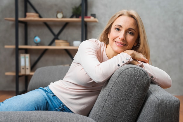 Portrait d&#39;une jeune femme souriante se penchant sur le canapé à la maison