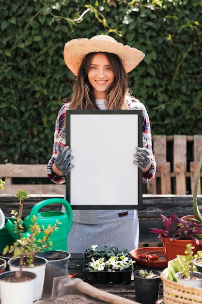 Photo gratuite portrait d'une jeune femme souriante tenant dans la main un cadre vierge blanc