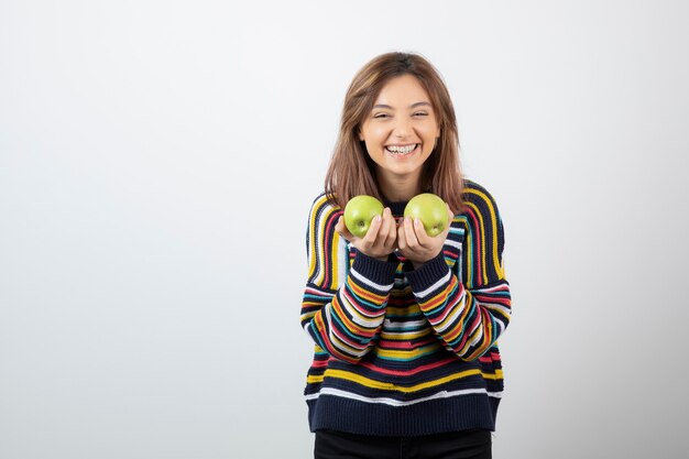 Portrait d'une jeune femme souriante tenant deux pommes vertes fraîches.