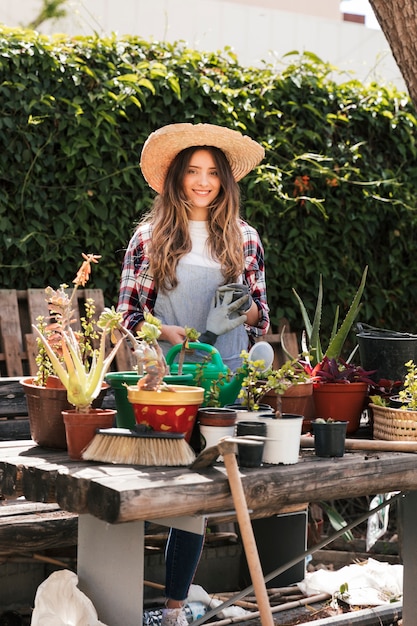 Photo gratuite portrait d'une jeune femme souriante tenant des gants de jardinage debout derrière les plantes sur table