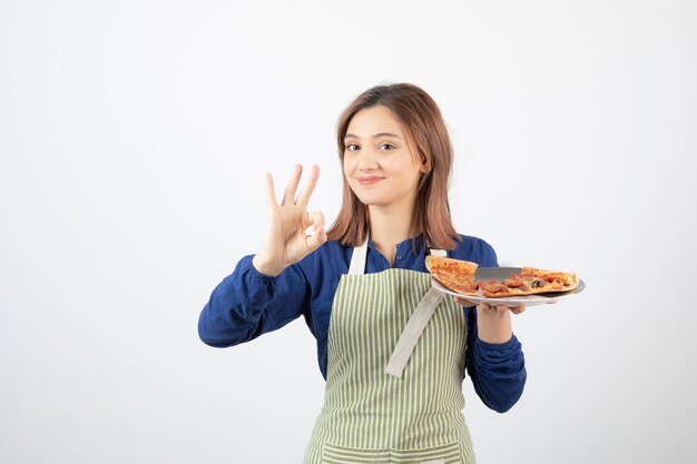 Portrait de jeune femme en tablier posant avec pizza sur blanc