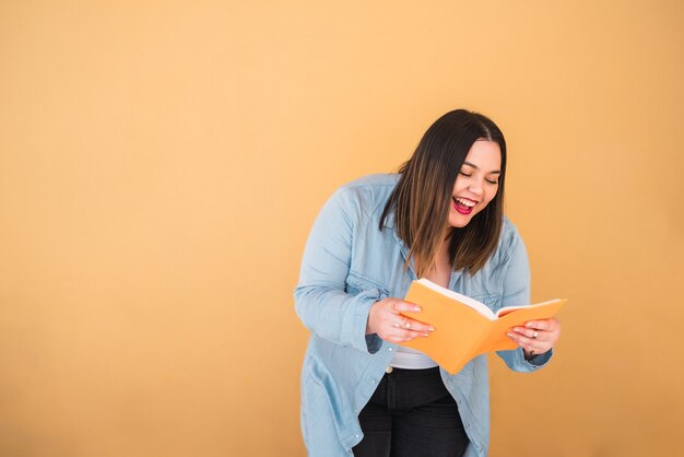 Portrait de jeune femme de taille plus appréciant le temps libre et lisant un livre en se tenant debout sur fond jaune. Concept de mode de vie.