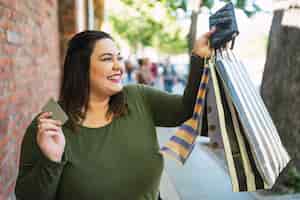 Photo gratuite portrait de jeune femme de taille plus tenant une carte de crédit et des sacs à provisions à l'extérieur dans la rue. concept d'achat et de vente.
