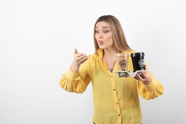 Portrait de jeune femme avec des tasses de café en regardant sa main sur fond blanc.