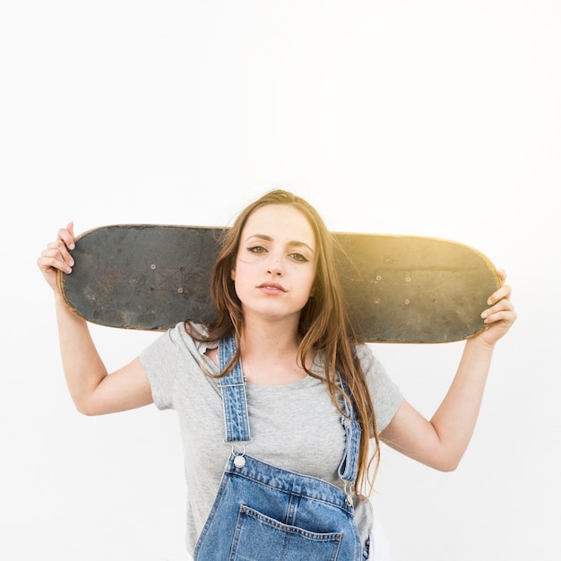 Portrait de jeune femme tenant une planche à roulettes par-dessus son épaule