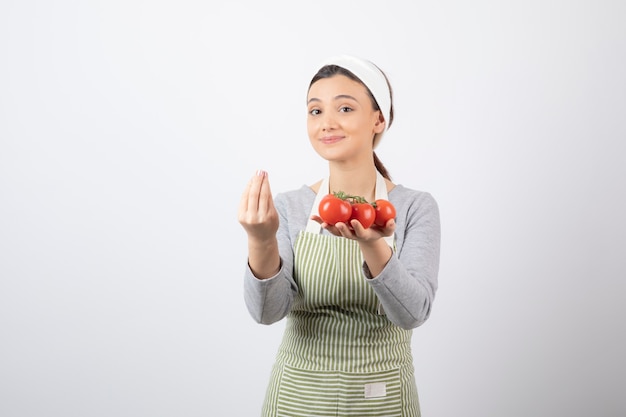 Portrait de jeune femme tenant des tomates rouges sur un mur blanc