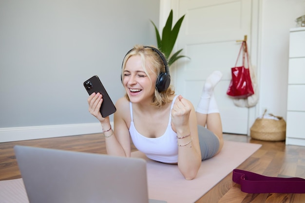 Photo gratuite portrait d'une jeune femme en train de faire de l'exercice en regardant des vidéos d'exercice sur un ordinateur portable dans des écouteurs allongés sur un tapis en caoutchouc